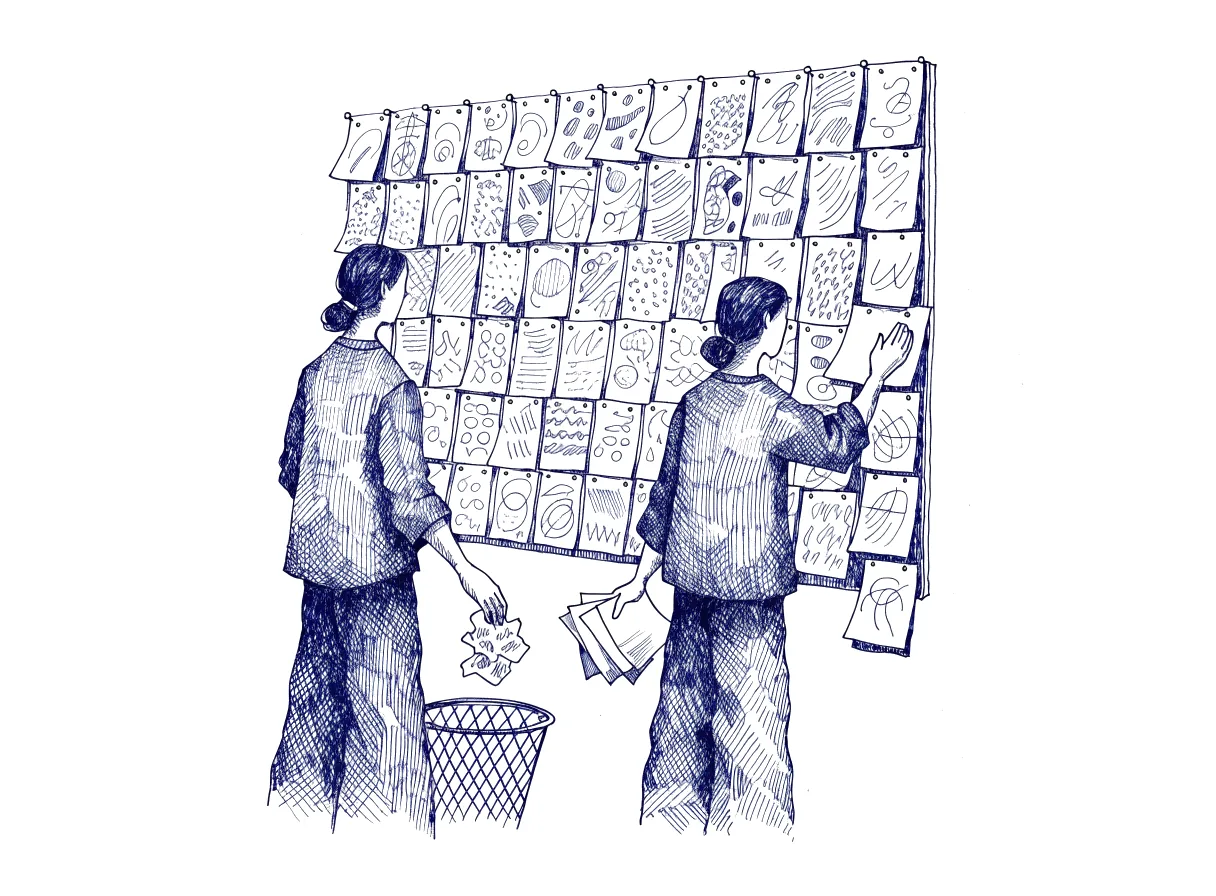 Two figures seen from behind, the backs of their heads showing, stand at a large pinboard of sketches, where one drops a crumpled sheet into a wire wastepaper basket and the other smooths out sheets taken from the basket and pins them in a separate column at the edge of the board, the whole scene drawn with wide empty margins on every side.